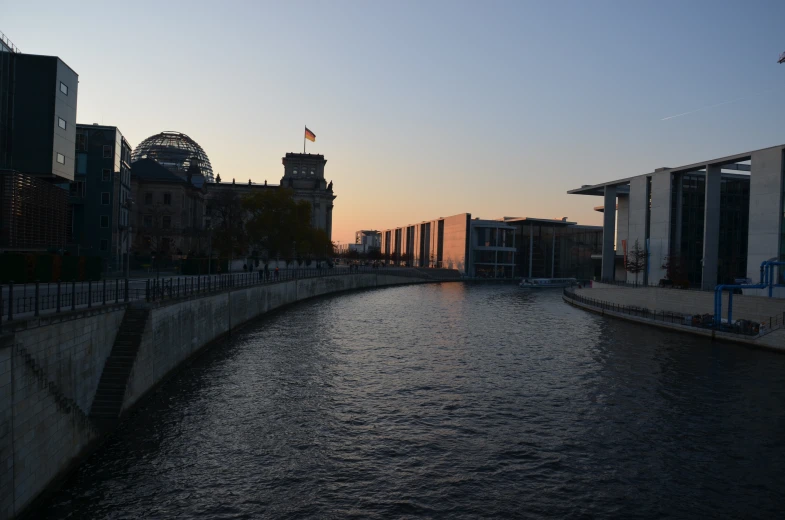 the sun rises on a river in front of buildings