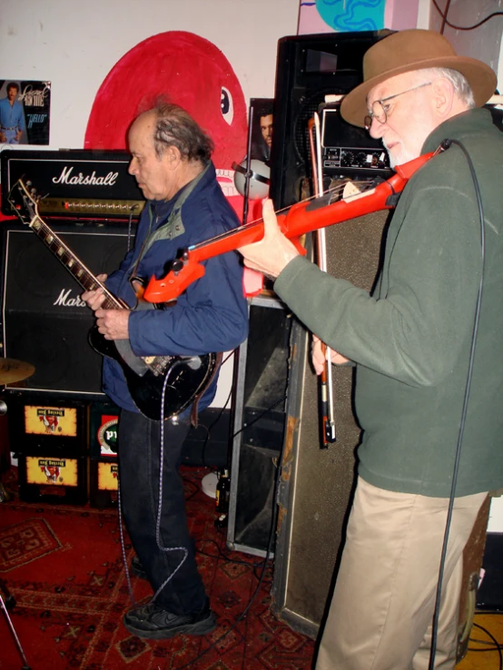 an older man playing the guitar next to an old man with a red beard