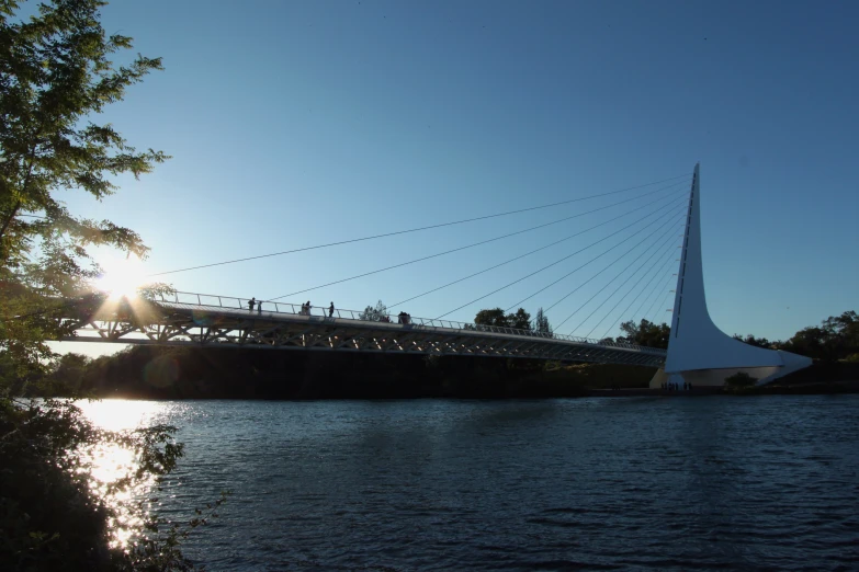 the sun is shining on a bridge near water