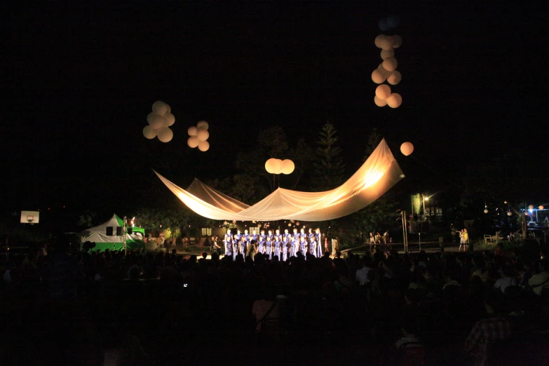 many lights illuminate balloons above a stage with white drap curtains and hanging lanterns