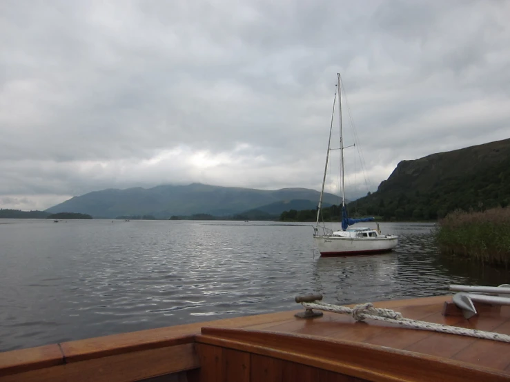 a sail boat floating on top of a lake next to a lush green hillside