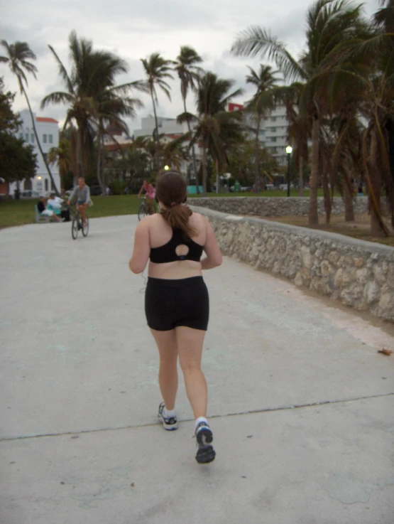 woman walking across cement roadway with palm trees in background