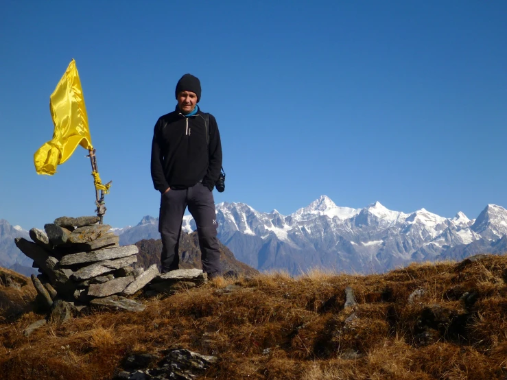 a man in black standing on top of a mountain with snow capped mountains behind him