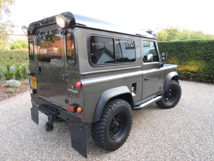 a land rover defender vehicle parked on gravel in front of bushes