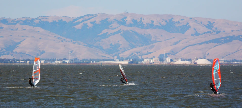three sail boarders with colorful sails out in the ocean