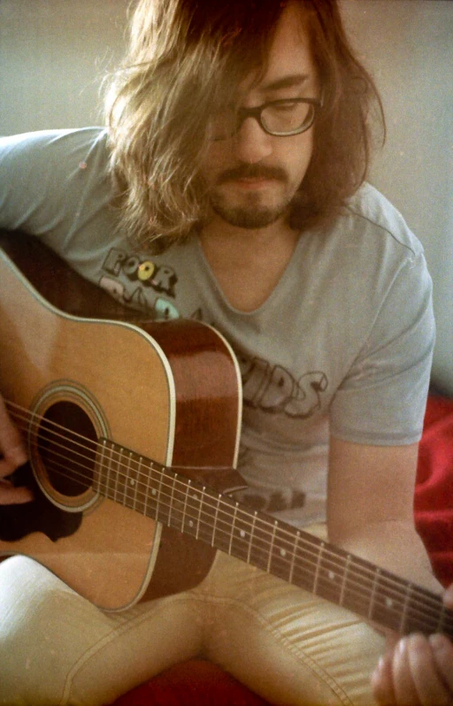 a man playing a guitar while sitting on top of a bed