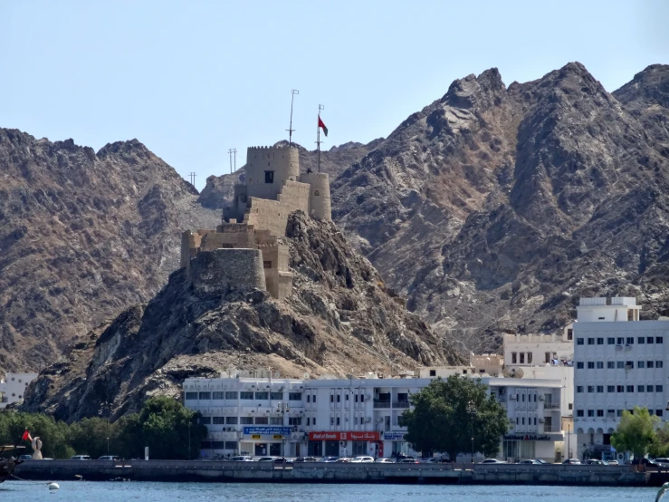 a large castle sits on a mountain near water