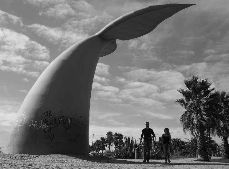 two people are riding their bikes near a large sculpture