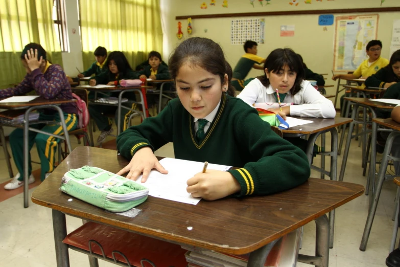 a school room filled with students and a girl writing on a book