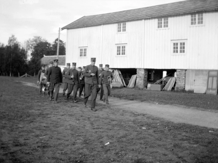 men in uniform walking down a dirt road next to a barn