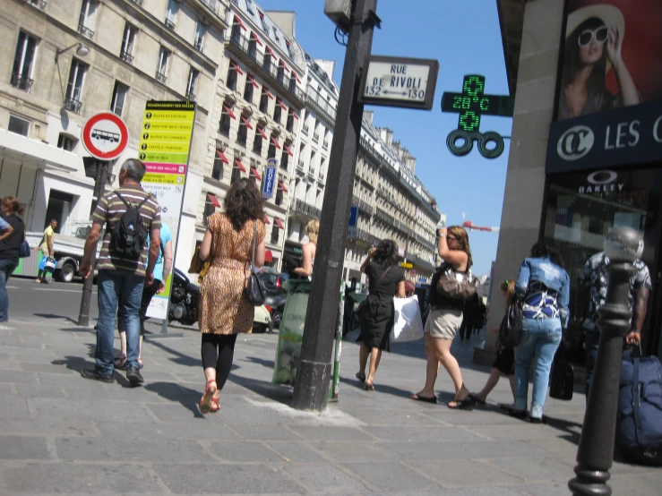 people walk on a street near pedestrians, street signs and stores