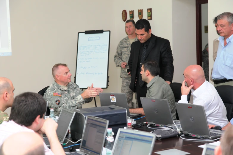 several military personnel standing at a conference room table