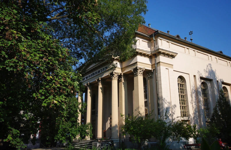 a large cream colored building has columns and trees