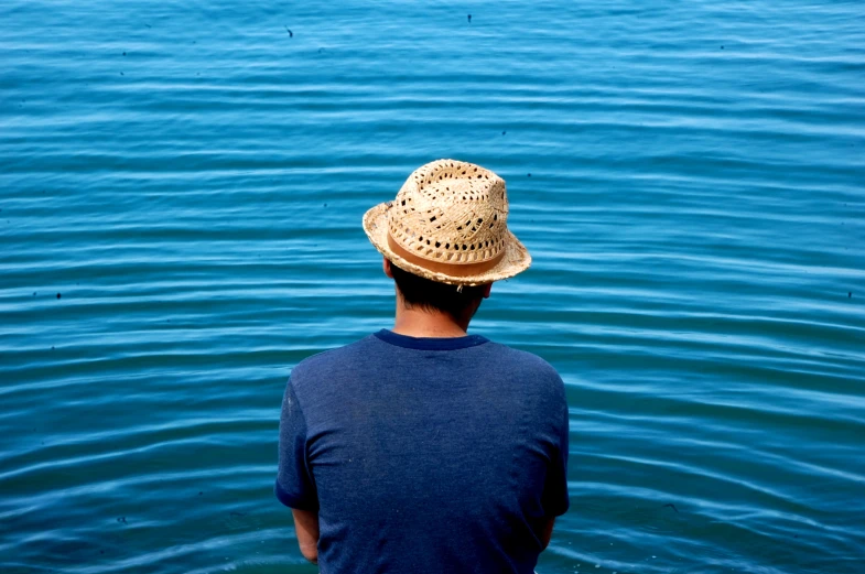 man in straw hat sitting on dock looking out into water