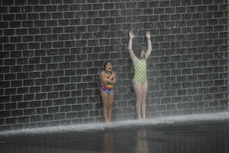 two young women stand by a waterfall in front of brick wall