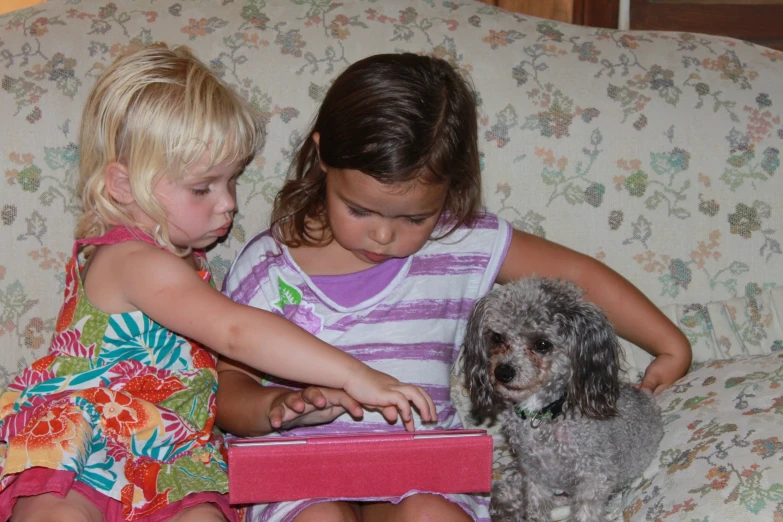 two little girls playing with their laptops while sitting on a couch