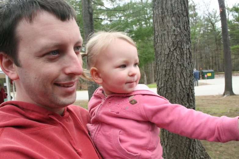 man holding up a baby in front of trees