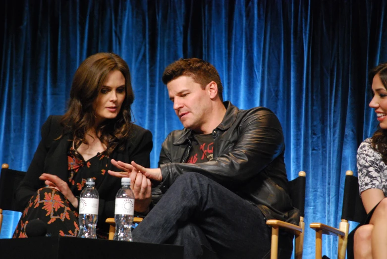 three people sitting down talking in front of a stage