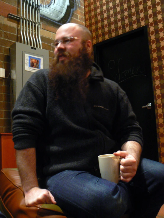 a man with a beard is sitting on a chair holding a coffee cup