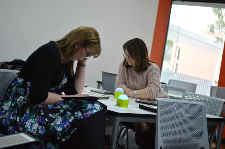 two women sitting at a table working on paper