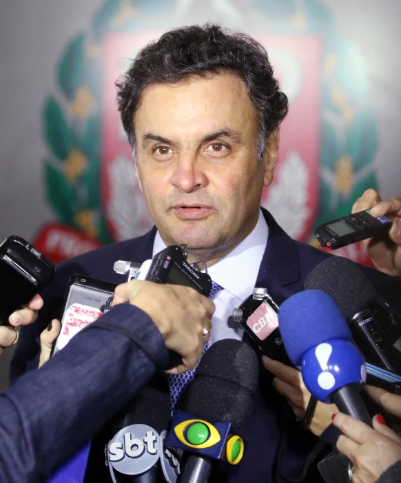 a man in suit and tie surrounded by microphones