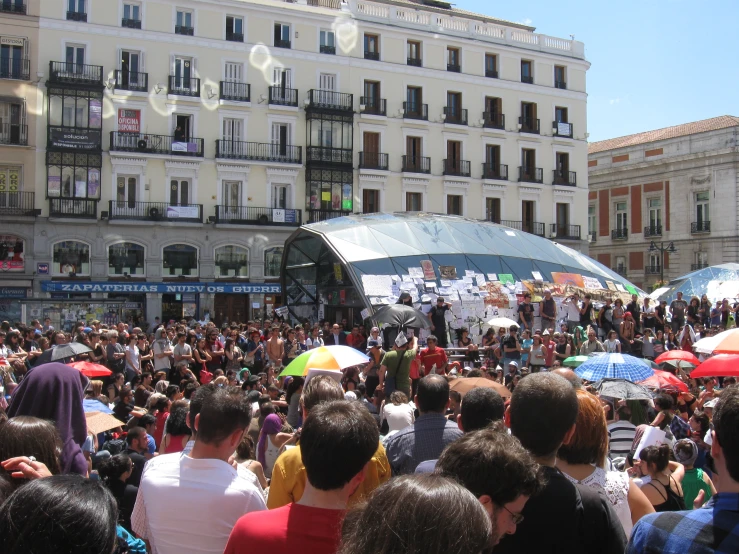 people stand and watch as one woman holds an umbrella