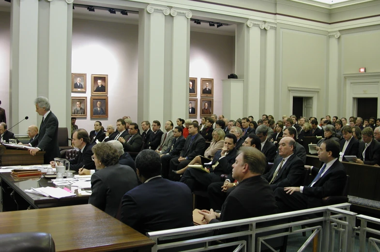 a large group of people in suits sitting down and listening to the lecturer