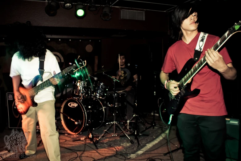 three young men playing guitar instruments with green light