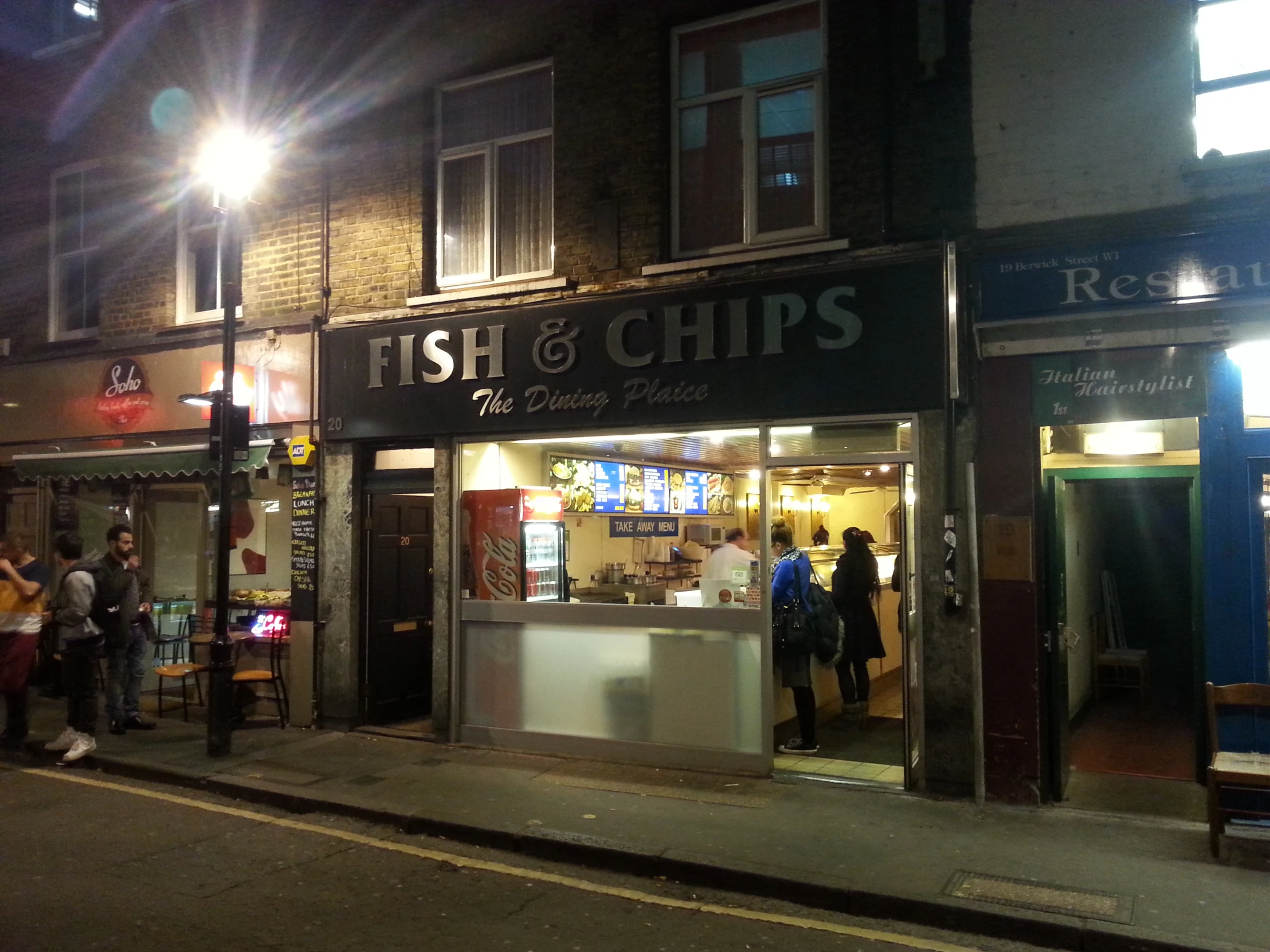 a restaurant at night with a couple of people standing in front