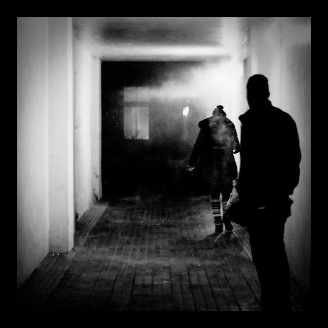 a man walking through a dark hallway carrying an umbrella
