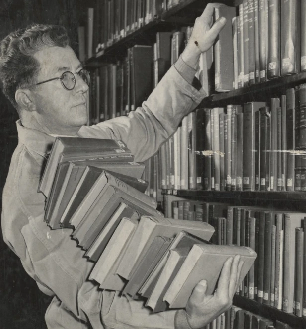 the man is picking up books from the book case