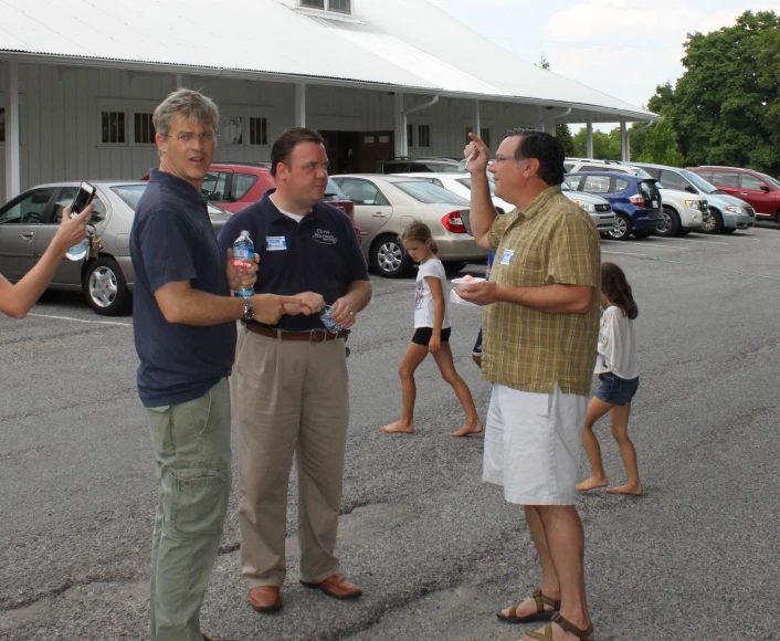 two men are talking and drinking with others in the background