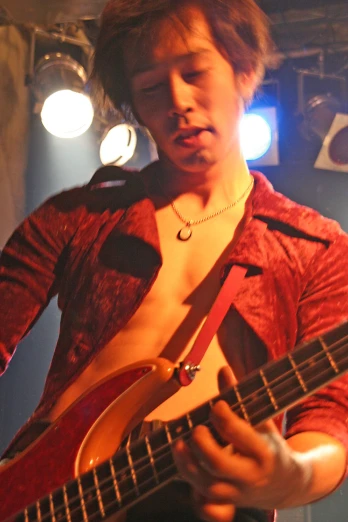 a man wearing red shirt playing guitar at concert