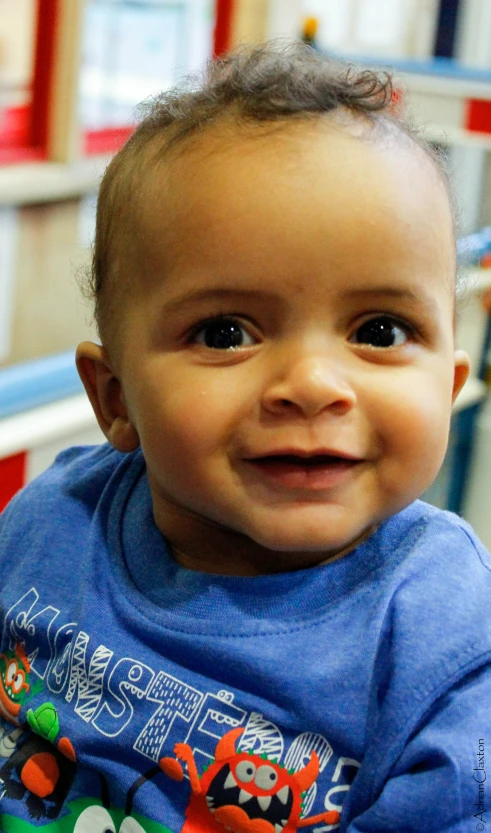 a baby boy smiling at the camera in front of a book shelf