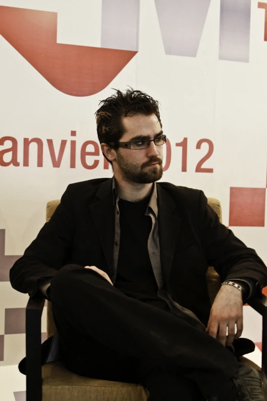 a man wearing glasses and a suit sitting in a chair