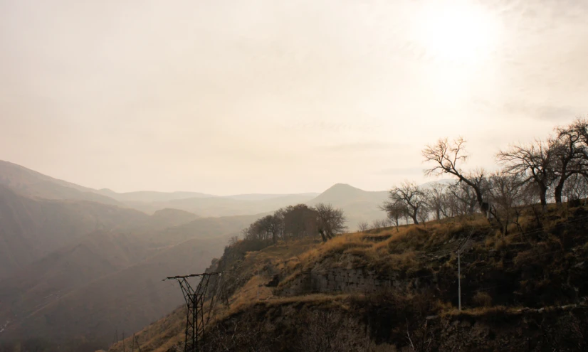 an area of brown grass and trees that are surrounded by mountains