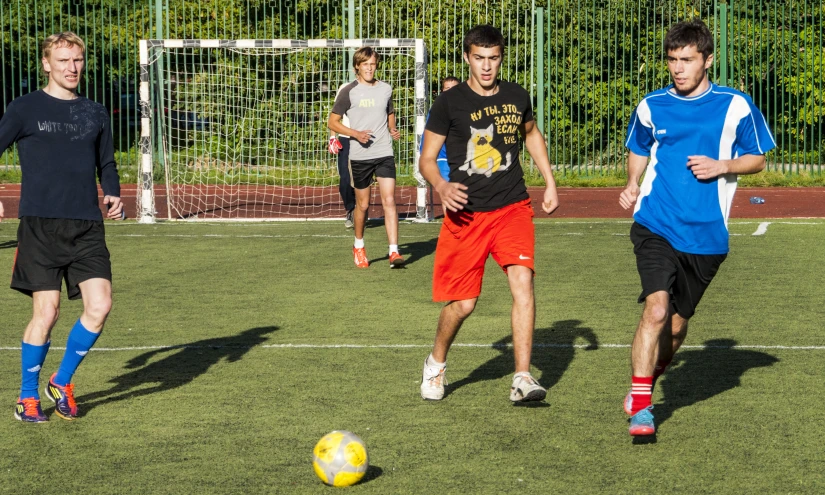 three men playing soccer on a field with one trying to kick the ball