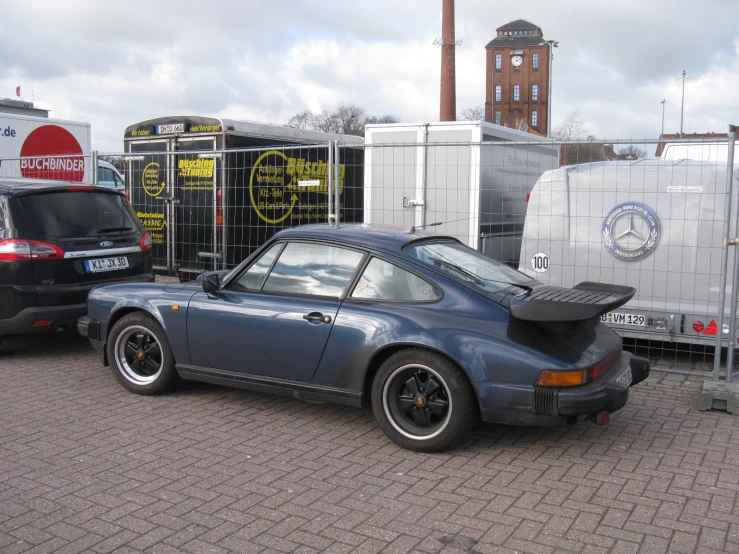 blue porsche 911 sits near other cars on a driveway