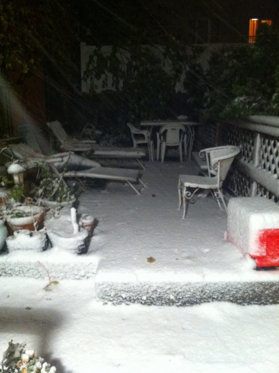 a view of a yard covered in snow, with several chairs and tables covered in snow