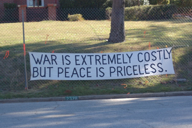a political sign near the curb with a sign that reads war is extremely possibly but peace is priceless