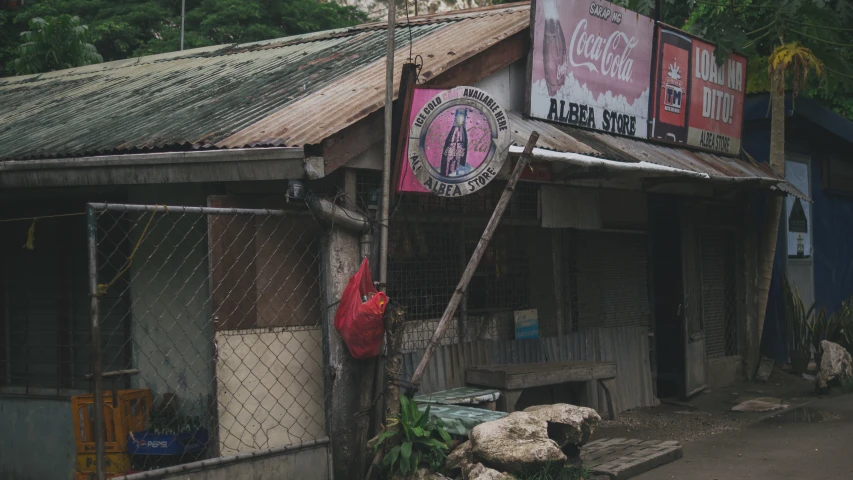 the building has signs on the front, a chain link fence behind and a plastic bag in the doorway