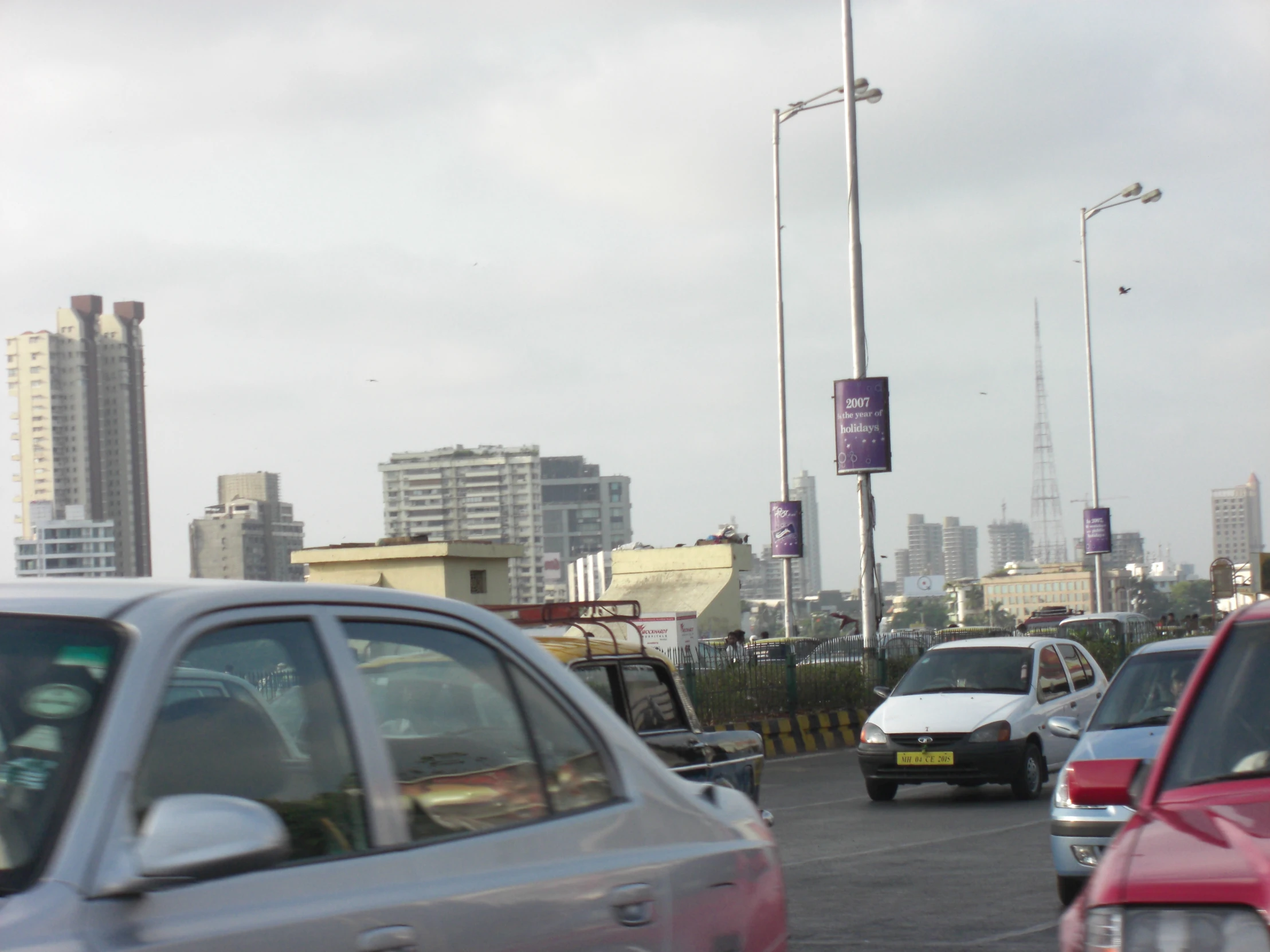 several cars drive down a busy street with a large city behind them