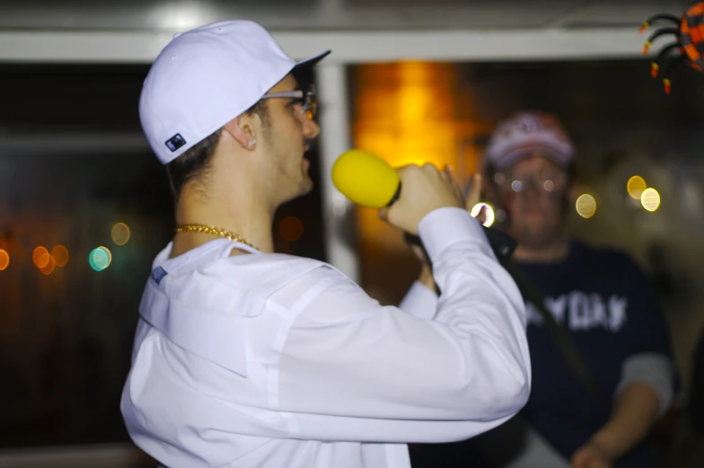 man in white shirt holding yellow object up to his face