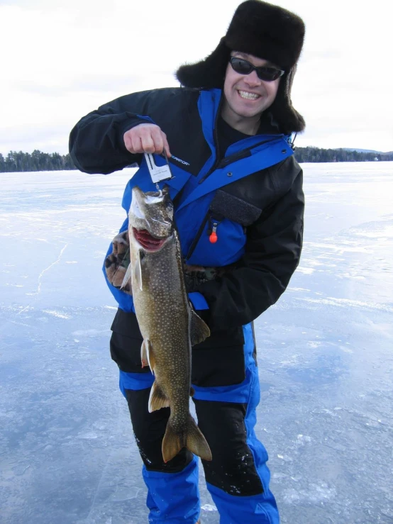 a man in sunglasses and a jacket holds a fish