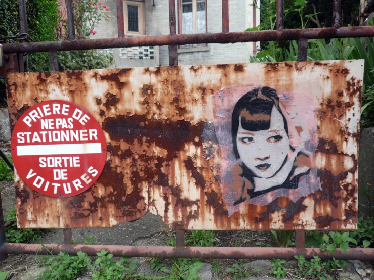 the sign is on a rusty fence that also shows a woman