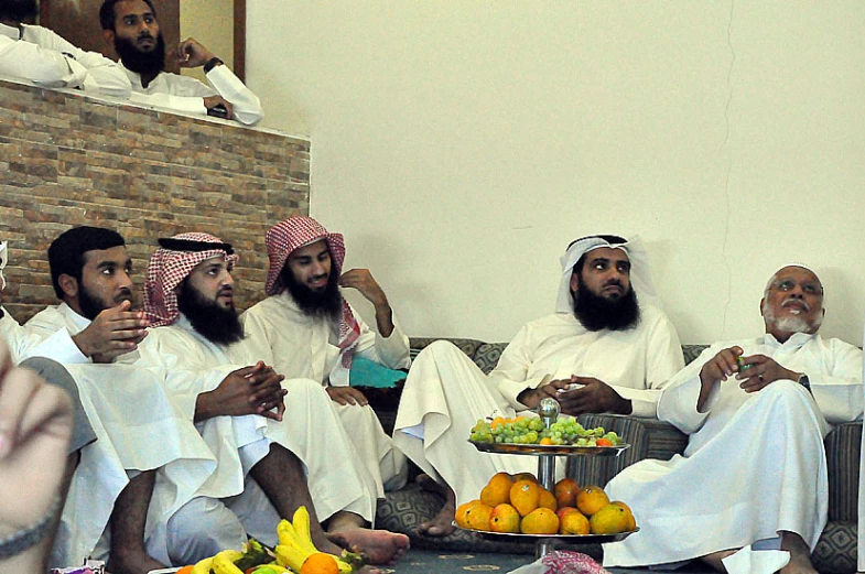 many men wearing white sit around with fruit