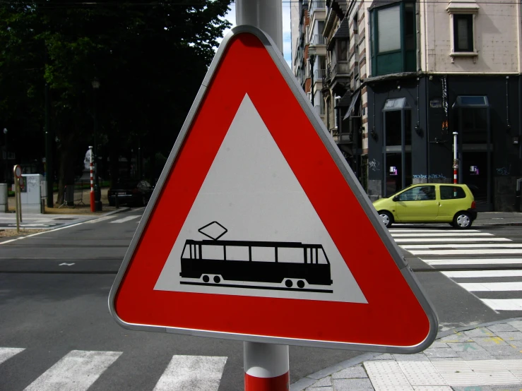 a sign showing bus on street with yellow car in background