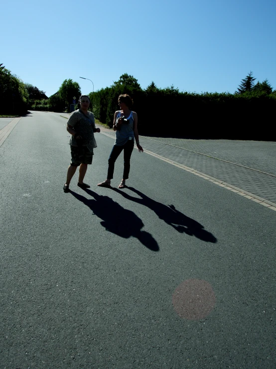two people on skateboards riding on an asphalt road