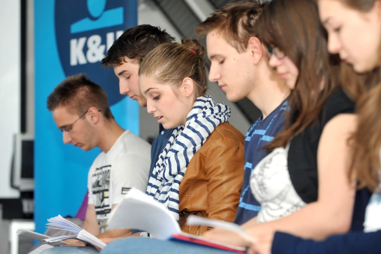 a row of students sit at a desk reading newspapers