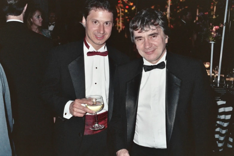 two men in tuxedos holding wine glasses